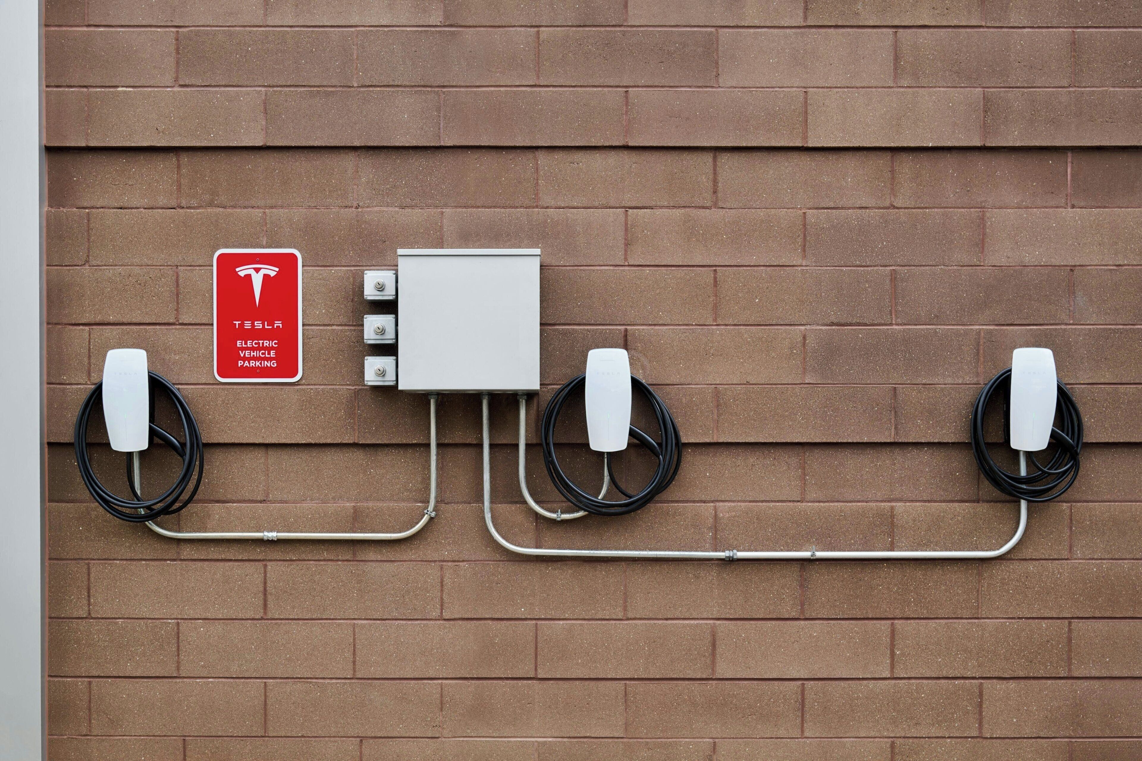 Señal de estacionamiento para vehículos Tesla eléctricos, estaciones de carga y un muro de ladrillo.