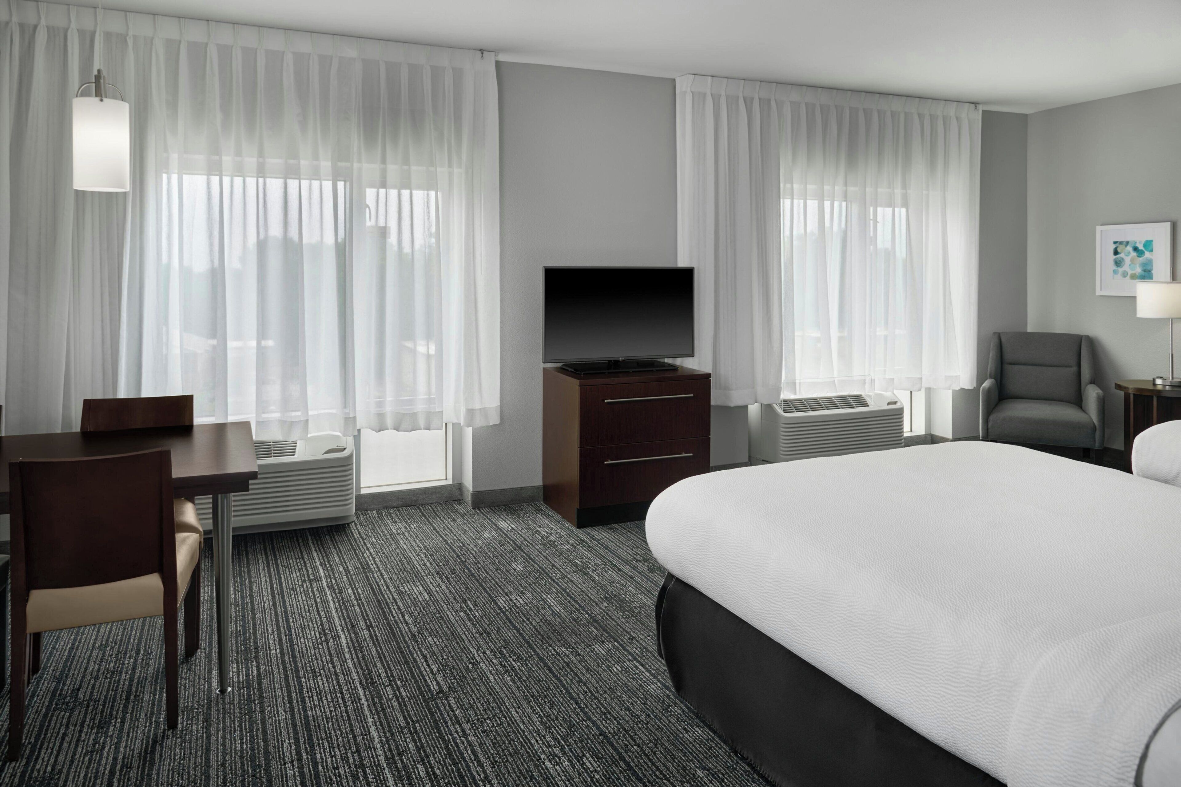 A hotel room with a bed, a TV, a desk, a chair, and a window with curtains.