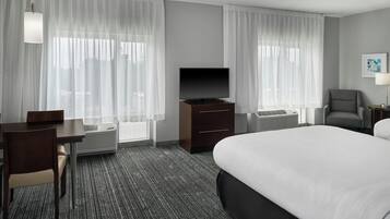 A hotel room with a bed, a TV, a desk, a chair, and a window with curtains.