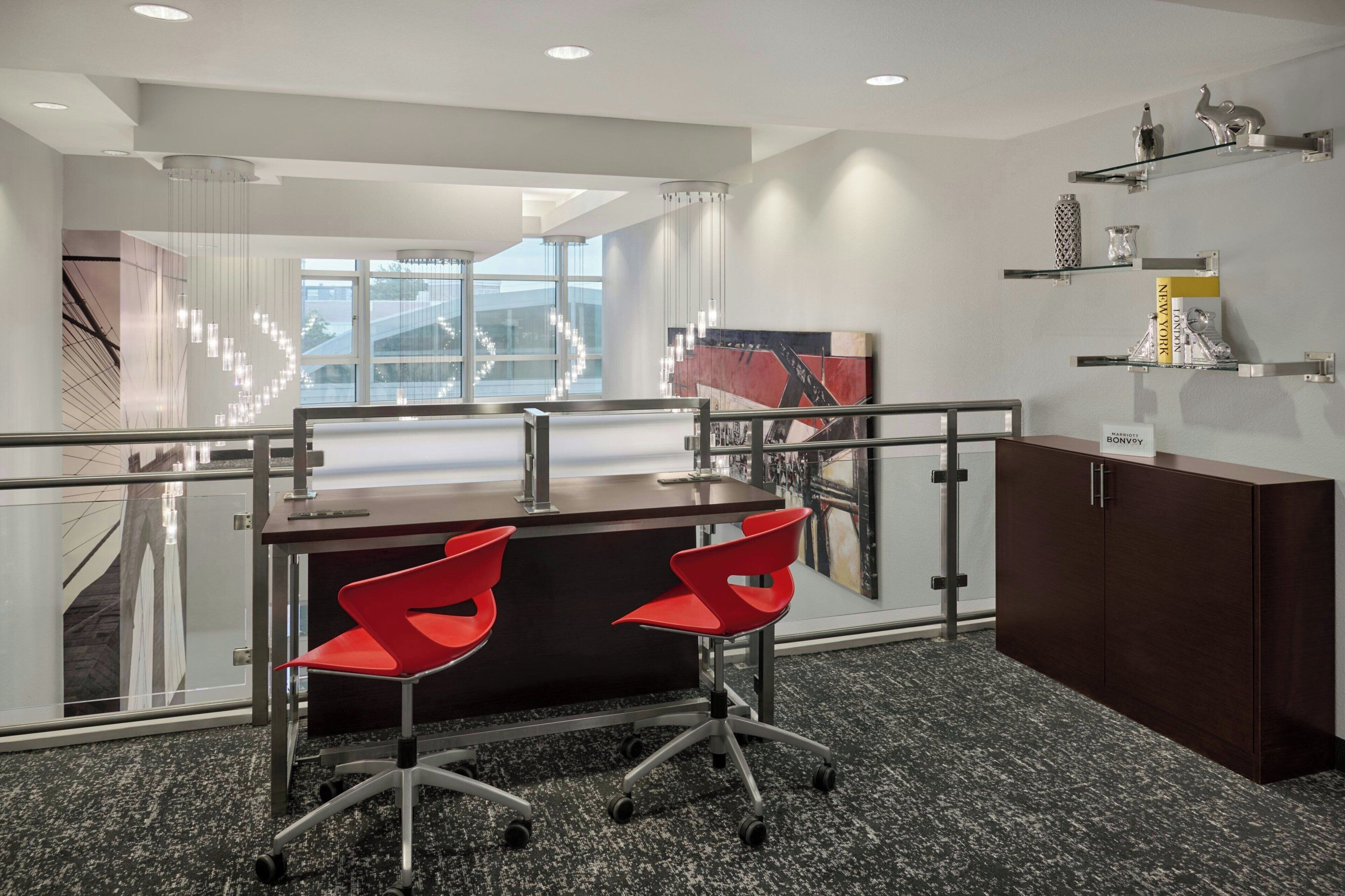 A modern office space with a desk, two red chairs, a dark wooden cabinet, and a glass railing.