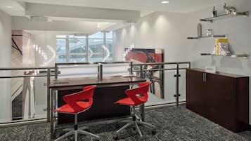 A modern office space with a desk, two red chairs, a dark wooden cabinet, and a glass railing.