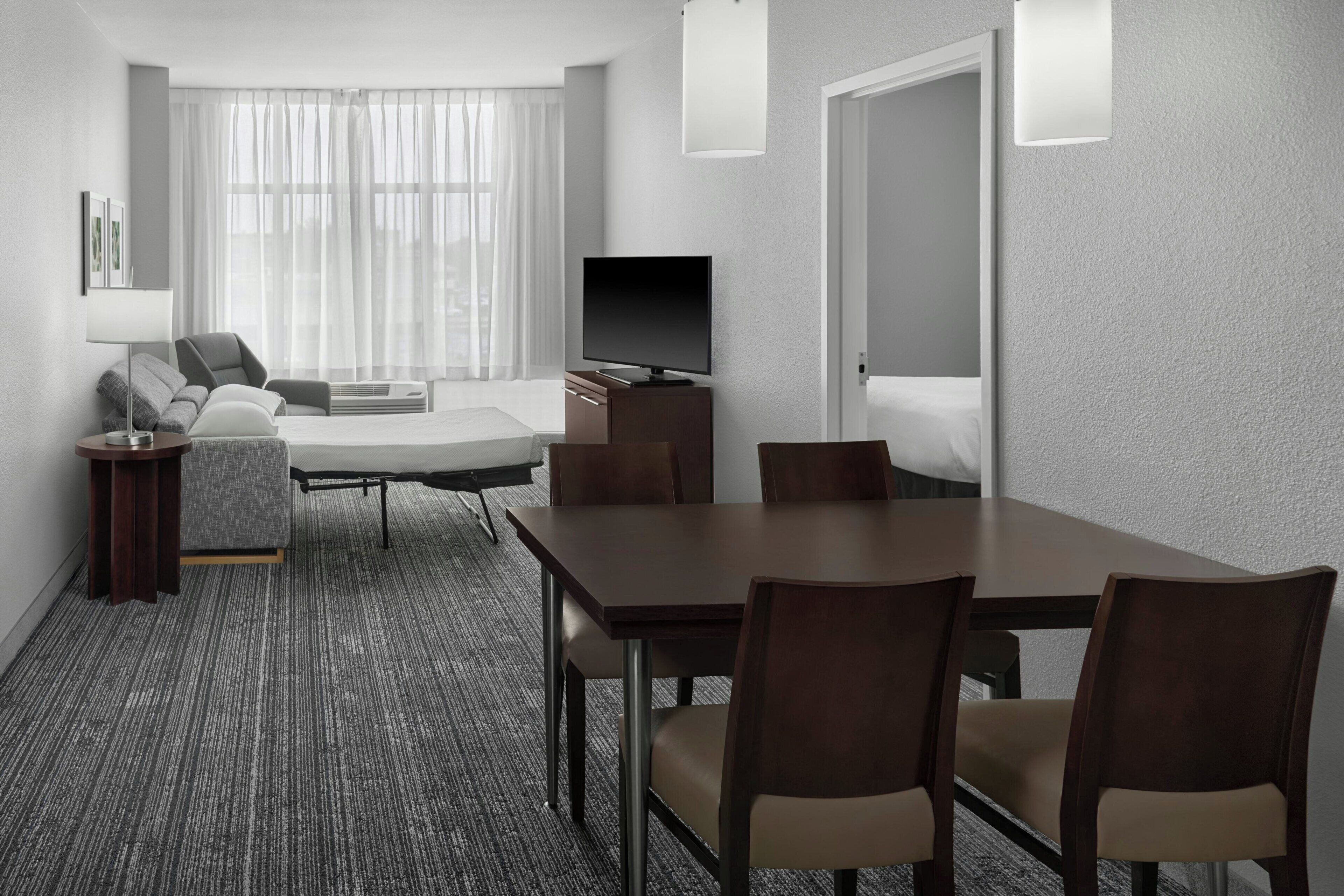 Een moderne hotelkamer met een groot bed, een televisie, een eettafel met stoelen, een bank en een klein bijzettafeltje.