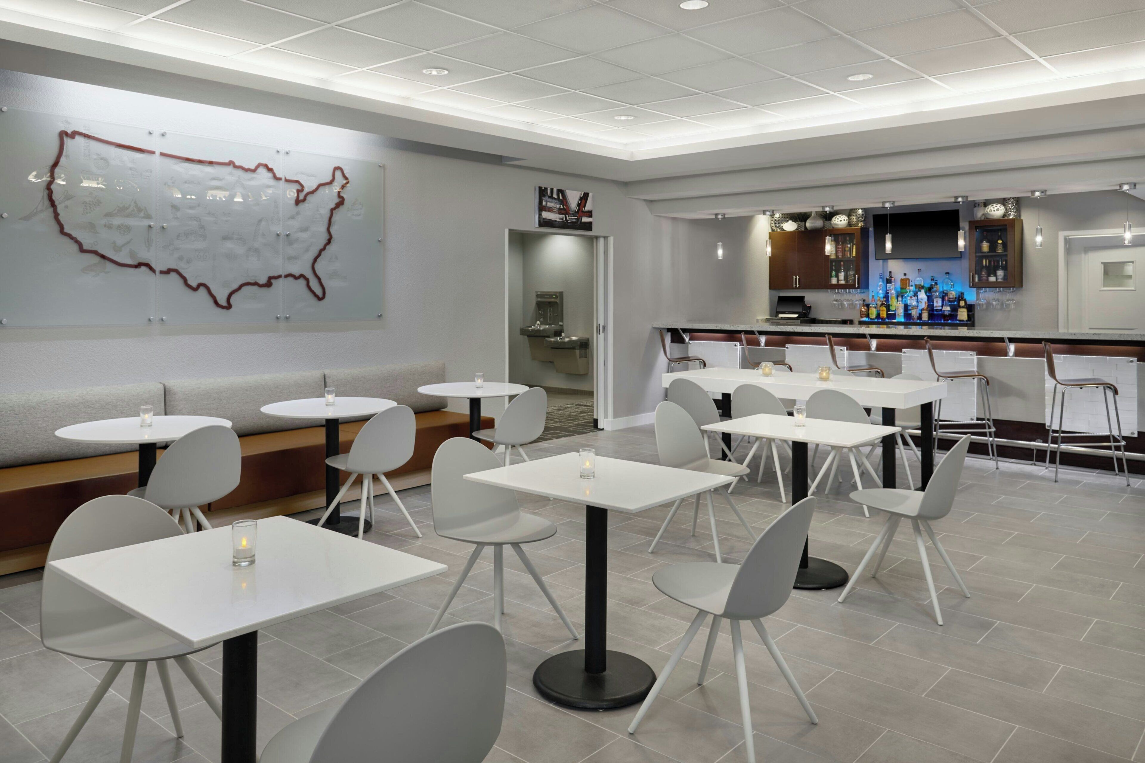A modern restaurant with white tables and chairs, a bar area, and a large wall map.