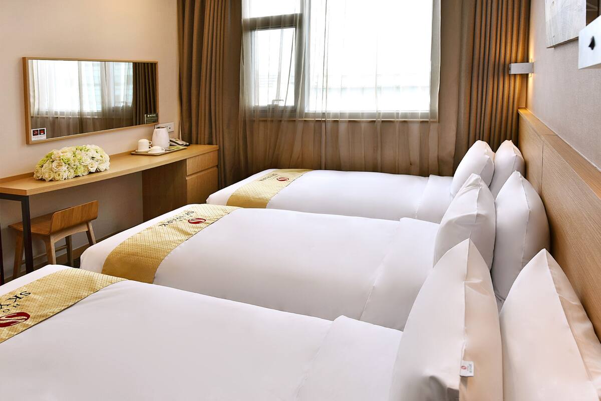 Une chambre d’hôtel avec deux lits, un bureau, une chaise, un miroir et une fenêtre avec des rideaux.