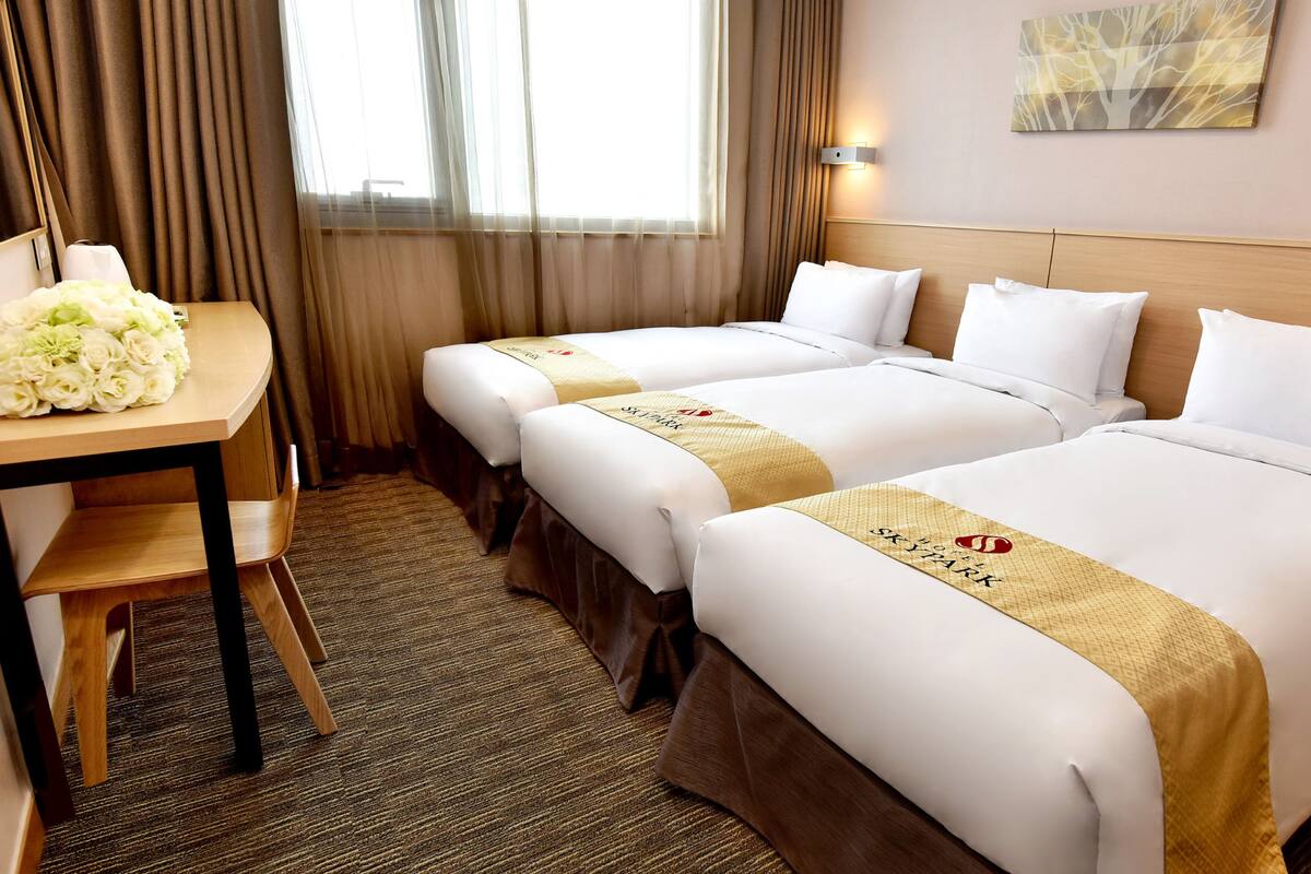 Une chambre d’hôtel avec deux lits, un bureau agrémenté d’un bouquet de fleurs et un luminaire fixé au mur.