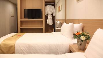 A hotel room with a bed, a TV, a robe, and a vase of flowers.