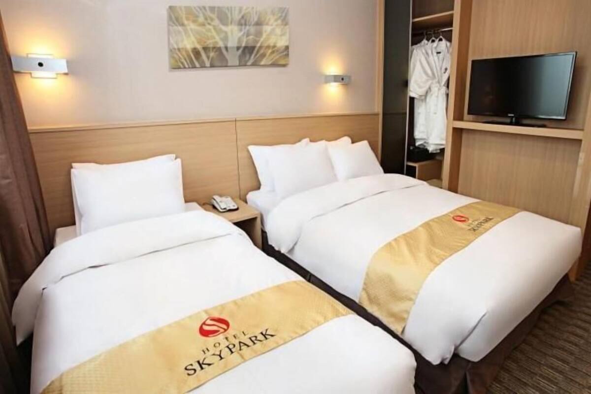 Une chambre d’hôtel avec deux lits, une télévision, une armoire et un tableau au mur.