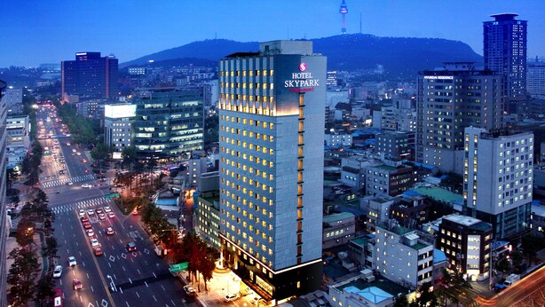 Un hotel moderno con varios pisos, un letrero llamativo y vistas de la ciudad circundante.