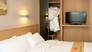 Habitación de hotel con cama, televisión, bata y armario con ropa colgada.