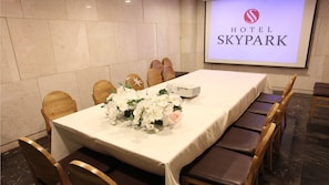Ein Hotelkonferenzraum mit einem langen Tisch, Stühlen und einer Projektionsleinwand, die den Namen des Hotels zeigt.