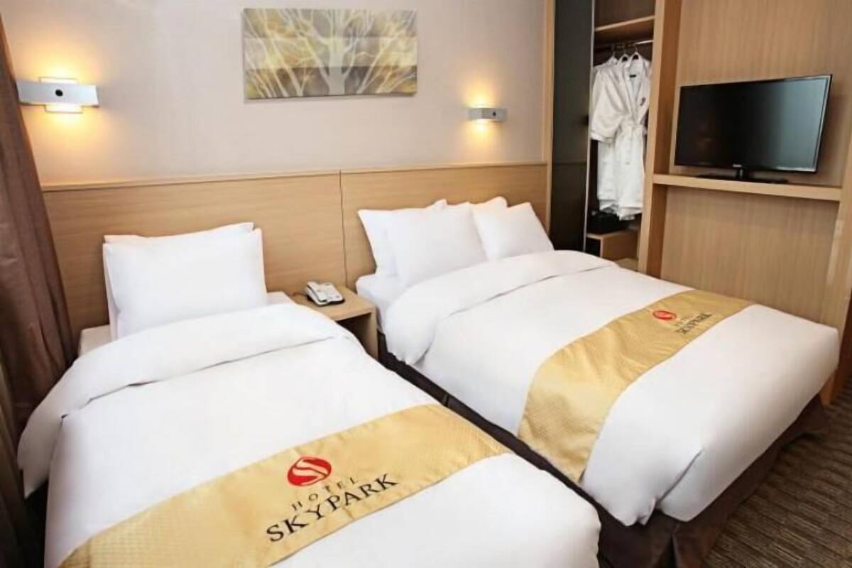 Une chambre d’hôtel avec deux lits, une télévision, une armoire et un tableau au mur.