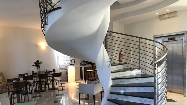 A modern interior with a spiral staircase, a reception desk, and a seating area with tables and chairs.