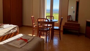 A hotel room with a bed, a dining table with chairs, a view of the outdoors, and a mirror on the wall.