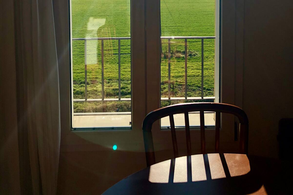 Ein Zimmer mit großem Fenster, einem Sessel und Blick auf ein grünes Feld.