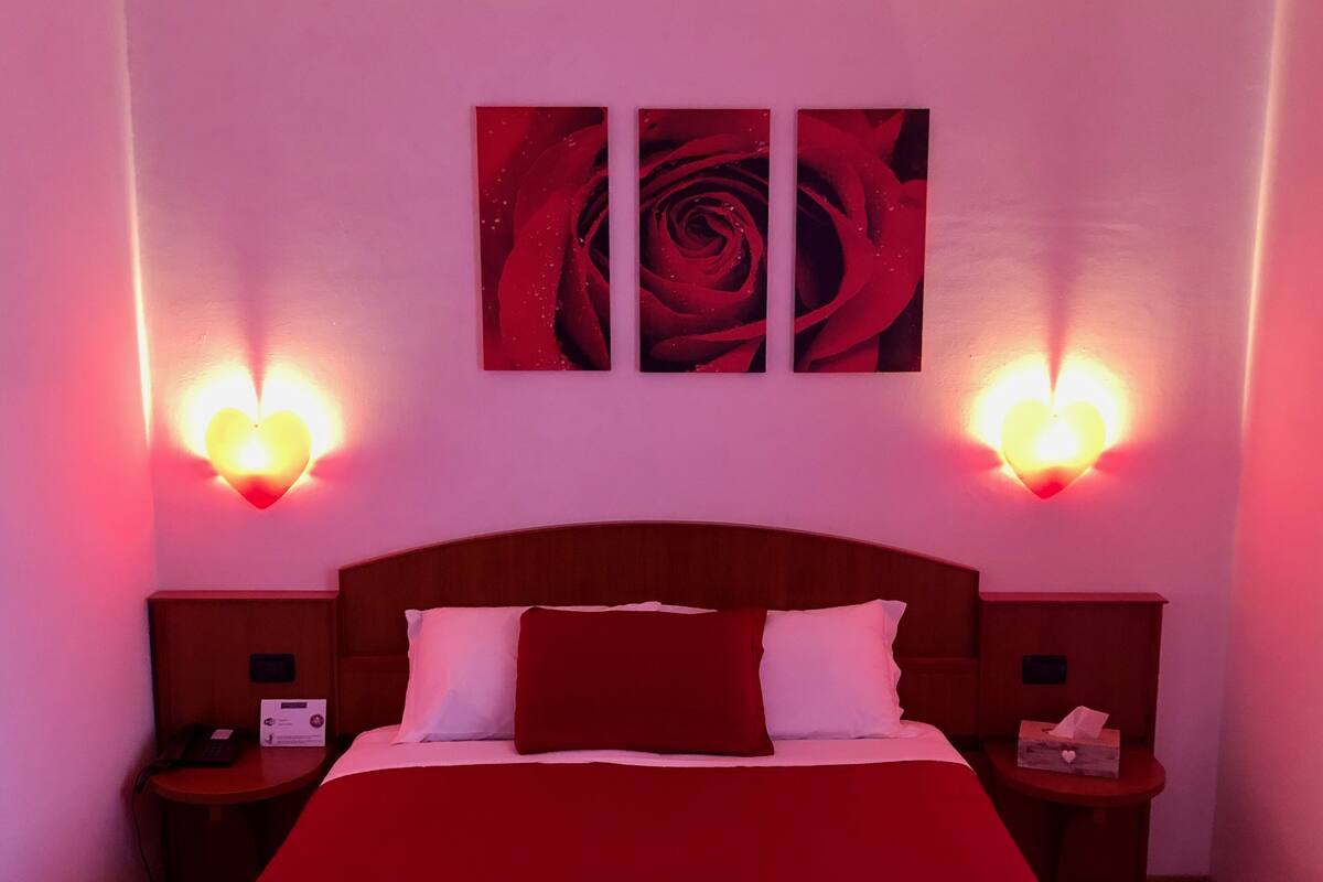 Ein Hotelzimmer mit einem großen Bett, zwei Nachttischen, einem Holzkopfstück und zwei herzförmigen Wandleuchten.