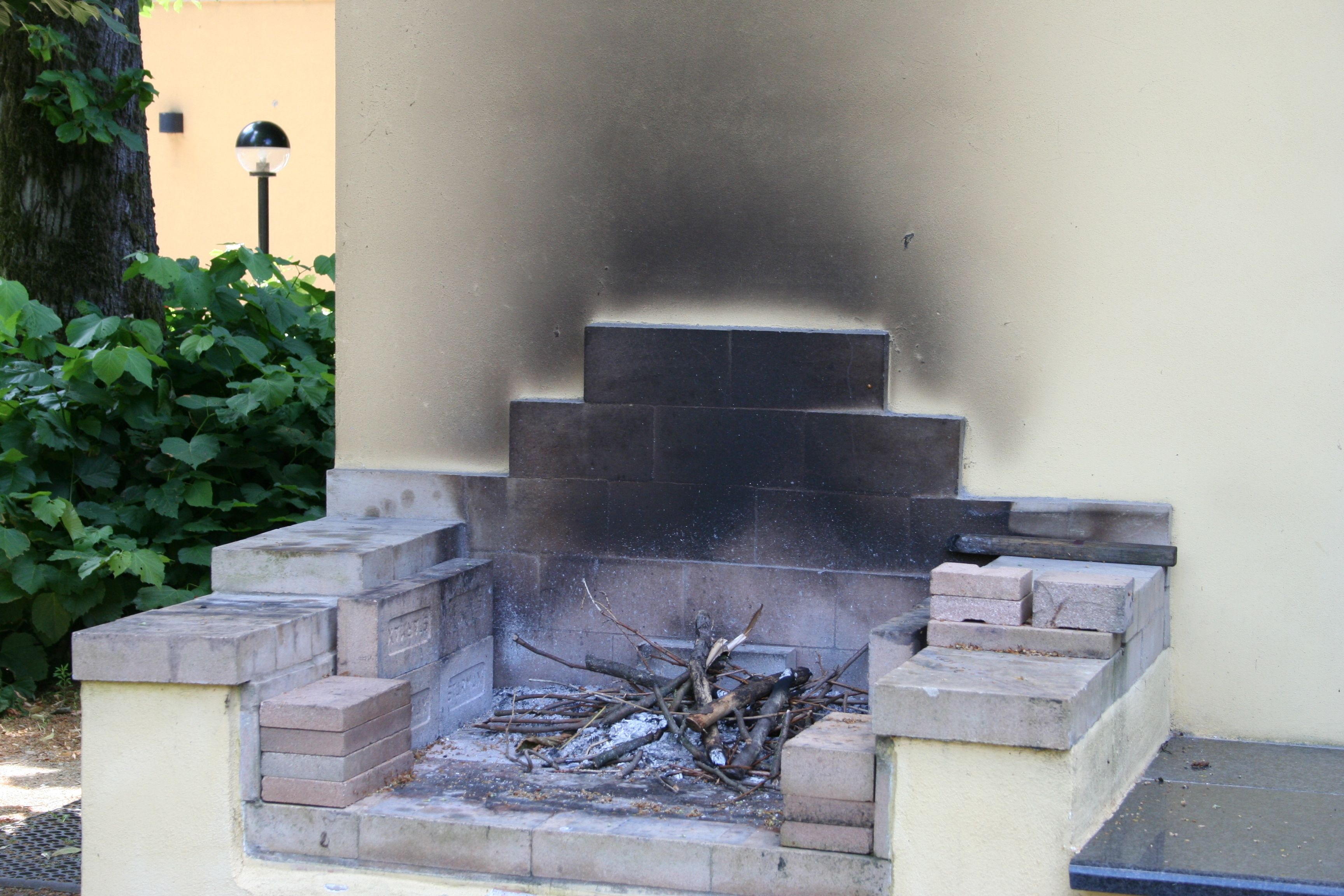 A stone-built outdoor fireplace with a fire, surrounded by steps and a wall.