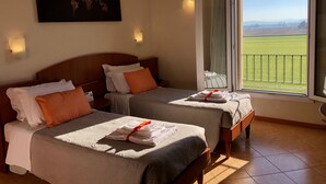 A hotel room with two beds, a world map artwork on the wall, and a balcony with a view of the countryside.