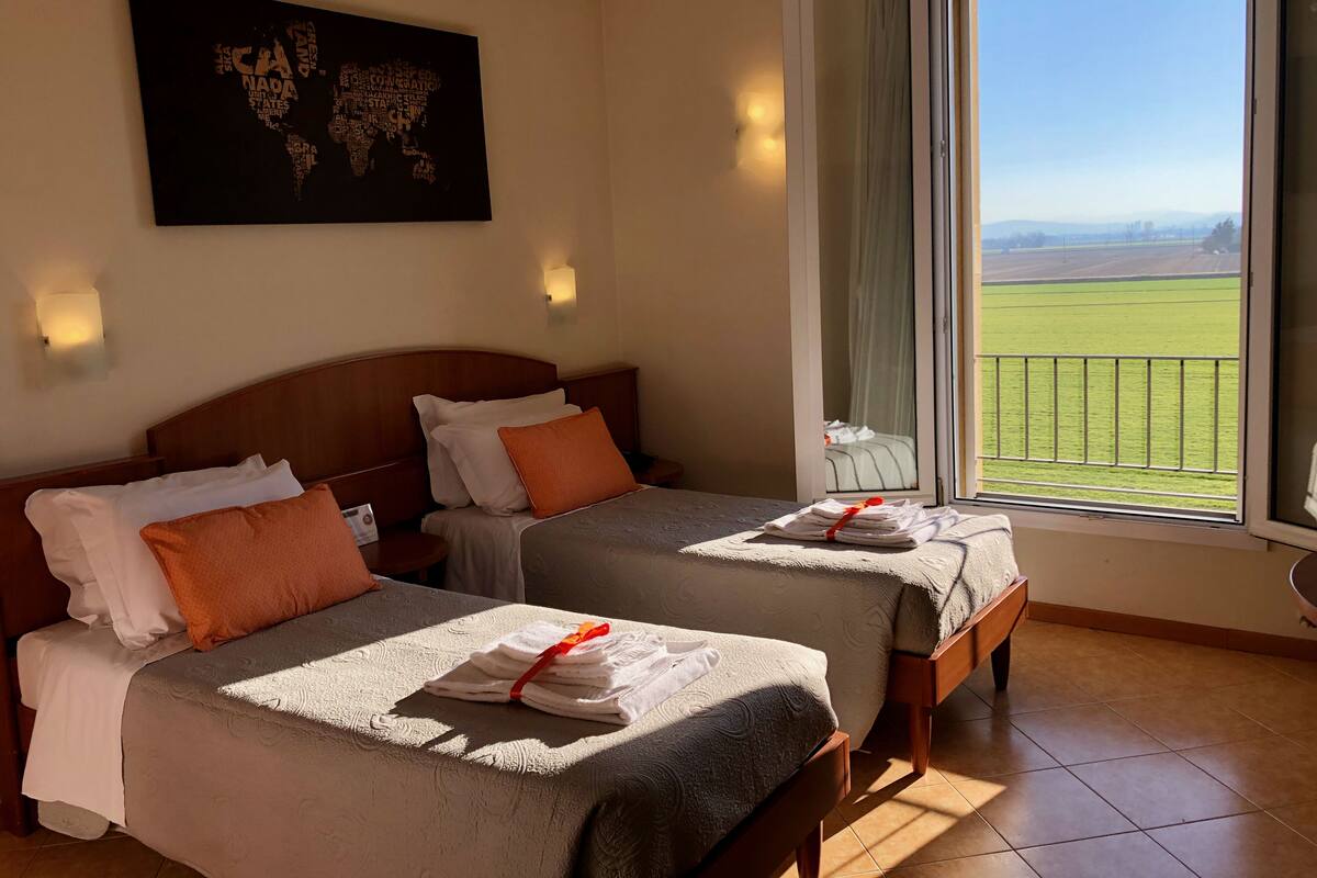 Ein Hotelzimmer mit zwei Betten, einer Weltkarte als Wandbild und einem Balkon mit Blick auf die Landschaft.