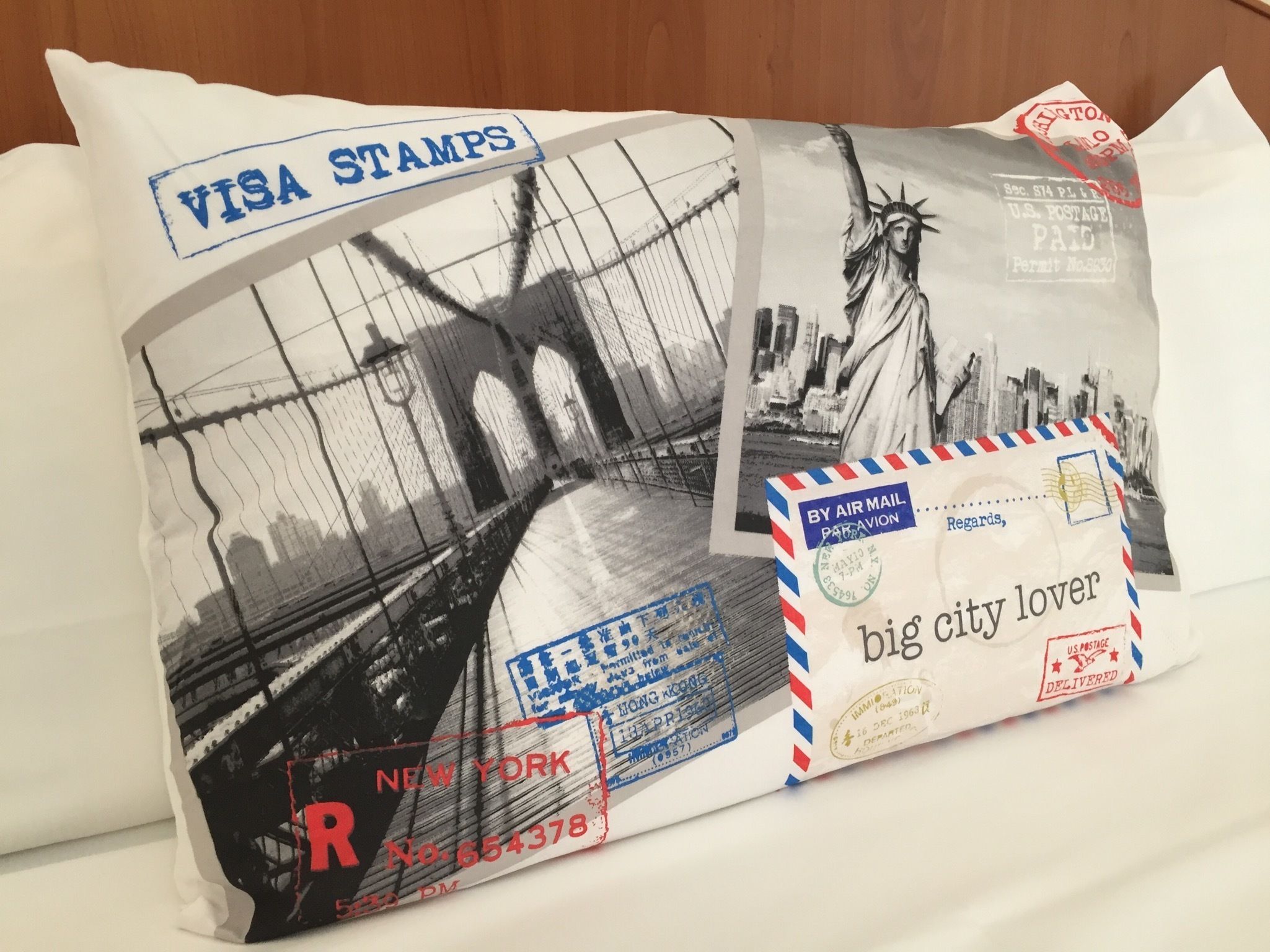 En kudde med ett svartvitt foto av Brooklyn Bridge och Frihetsgudinnan, ett vykort med en stadsbild och ett brev med ett rött frimärke.