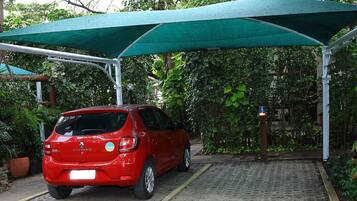 Un auto rojo estacionado bajo un toldo verde en un estacionamiento techado con un camino adoquinado.