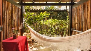 Een hangmat onder een houten pergola met een tafel en stoelen, omgeven door weelderige begroeiing.