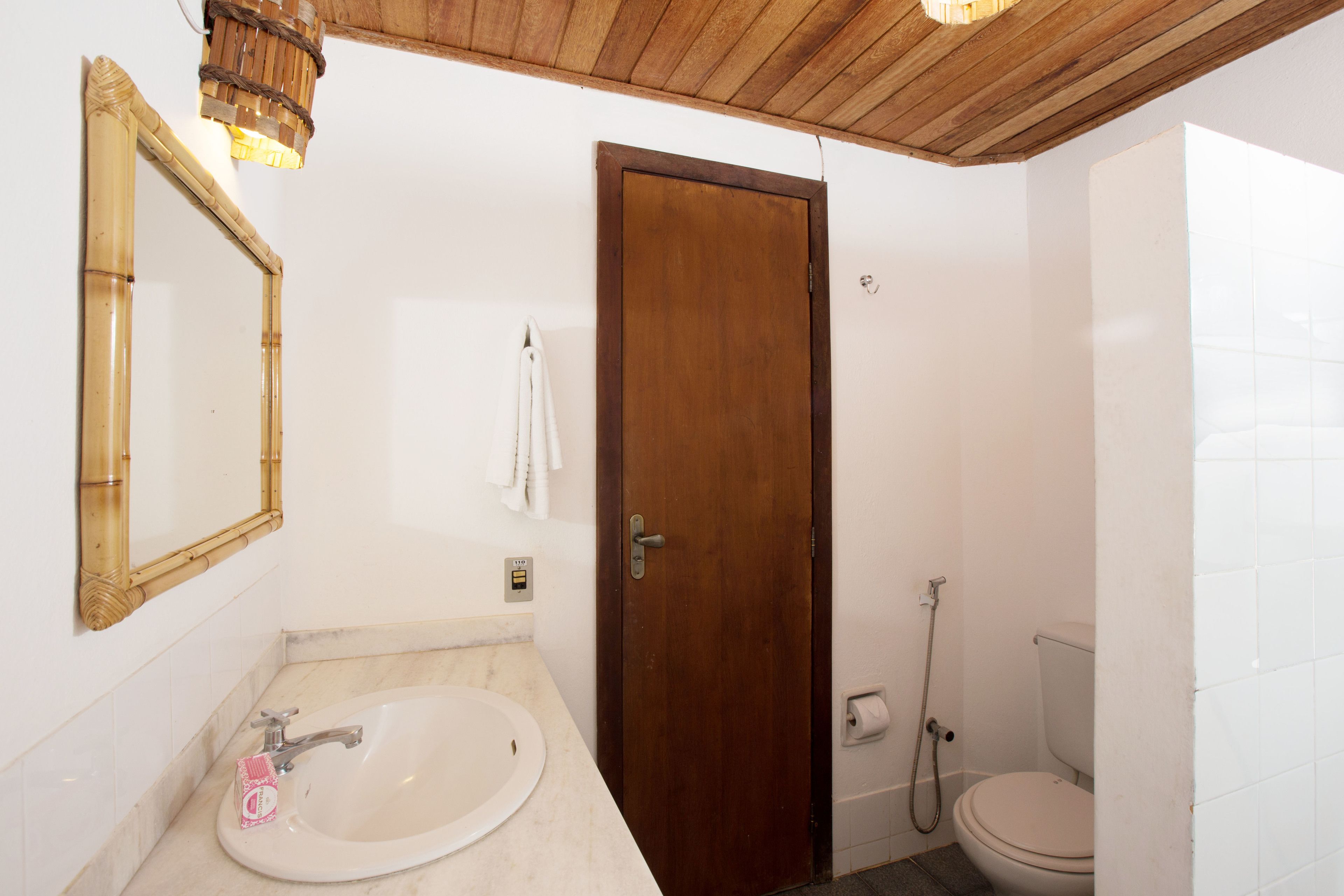 Une salle de bain avec une porte en bois, un lavabo avec un robinet, des toilettes et un miroir avec un cadre en bois.