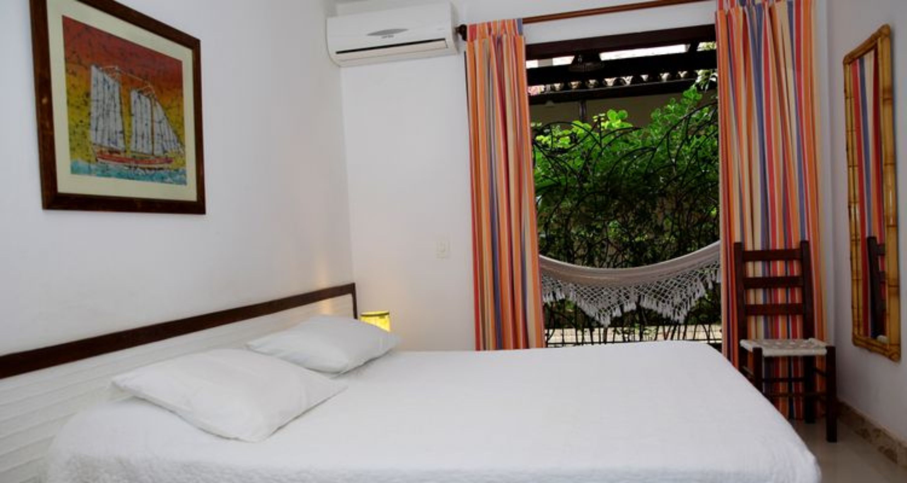 A bedroom with a bed, a hammock, a hammock chair, a bookshelf, and a painting on the wall.