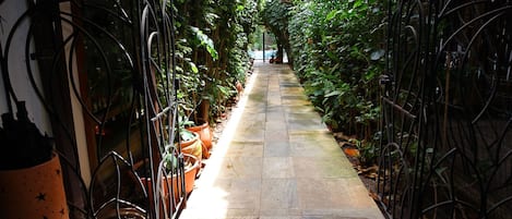 Un sendero estrecho flanqueado por una verja metálica, que conduce a una puerta con un felpudo que dice "Oogum Marinho".