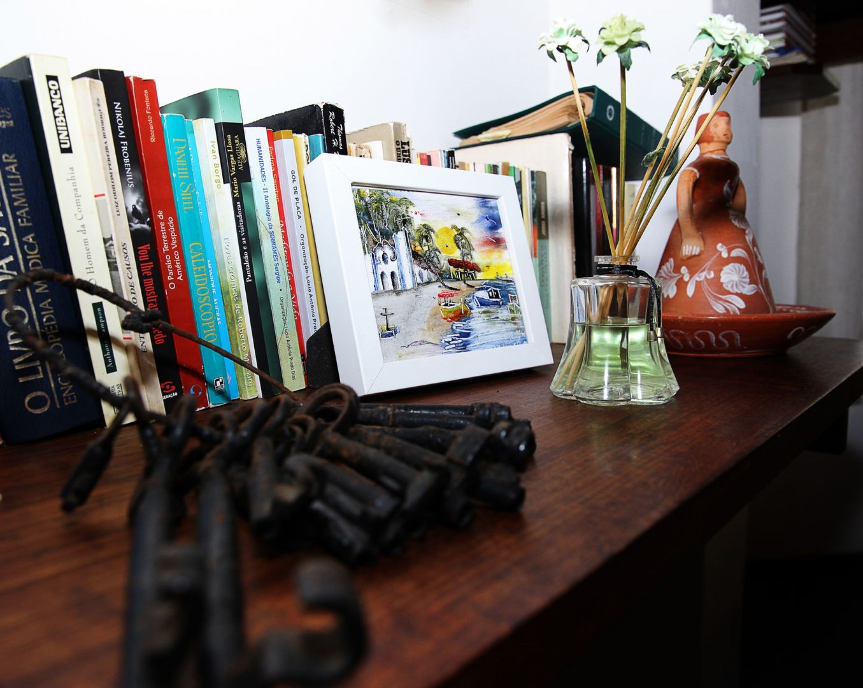 A desk with books, a framed picture, a vase with flowers, and a pair of glasses.
