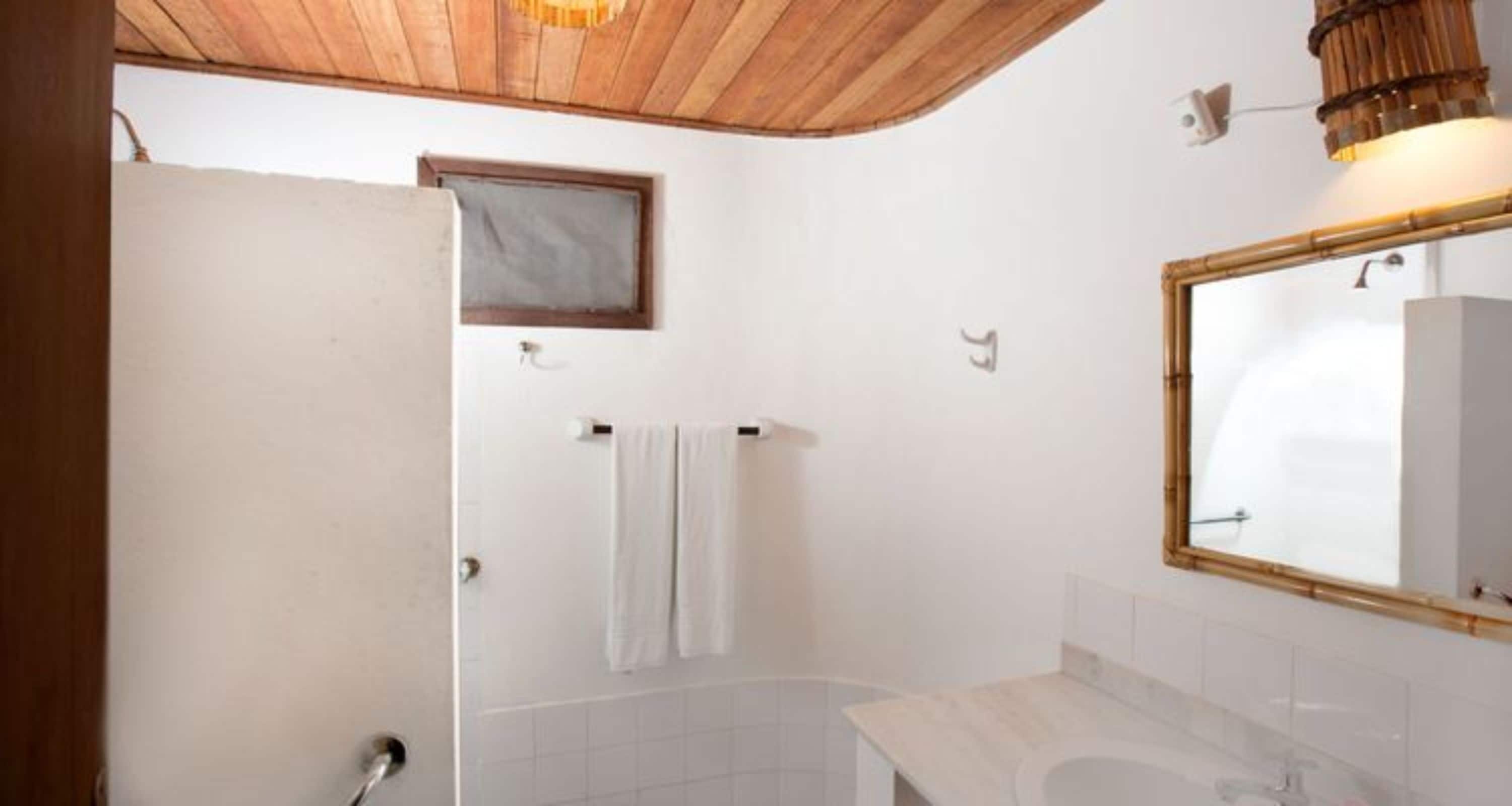 Un baño con techo de madera, un lavabo blanco, un espejo y un perchero para toallas.