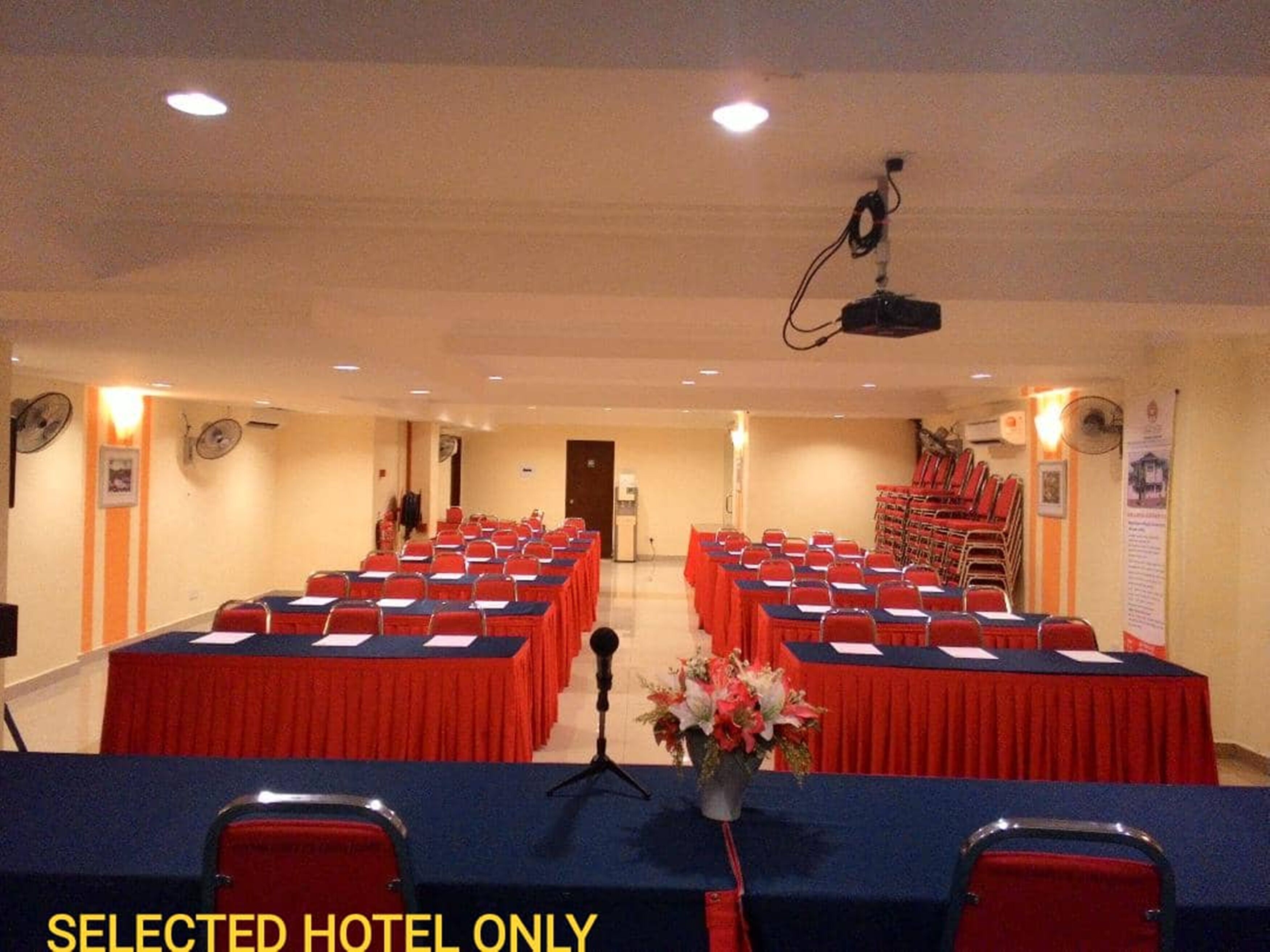 A conference room with rows of tables and chairs, a podium, and a projector.