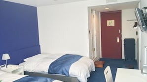 Une chambre d’hôtel avec deux lits, un bureau, une chaise, une télévision et une porte donnant sur une autre pièce.