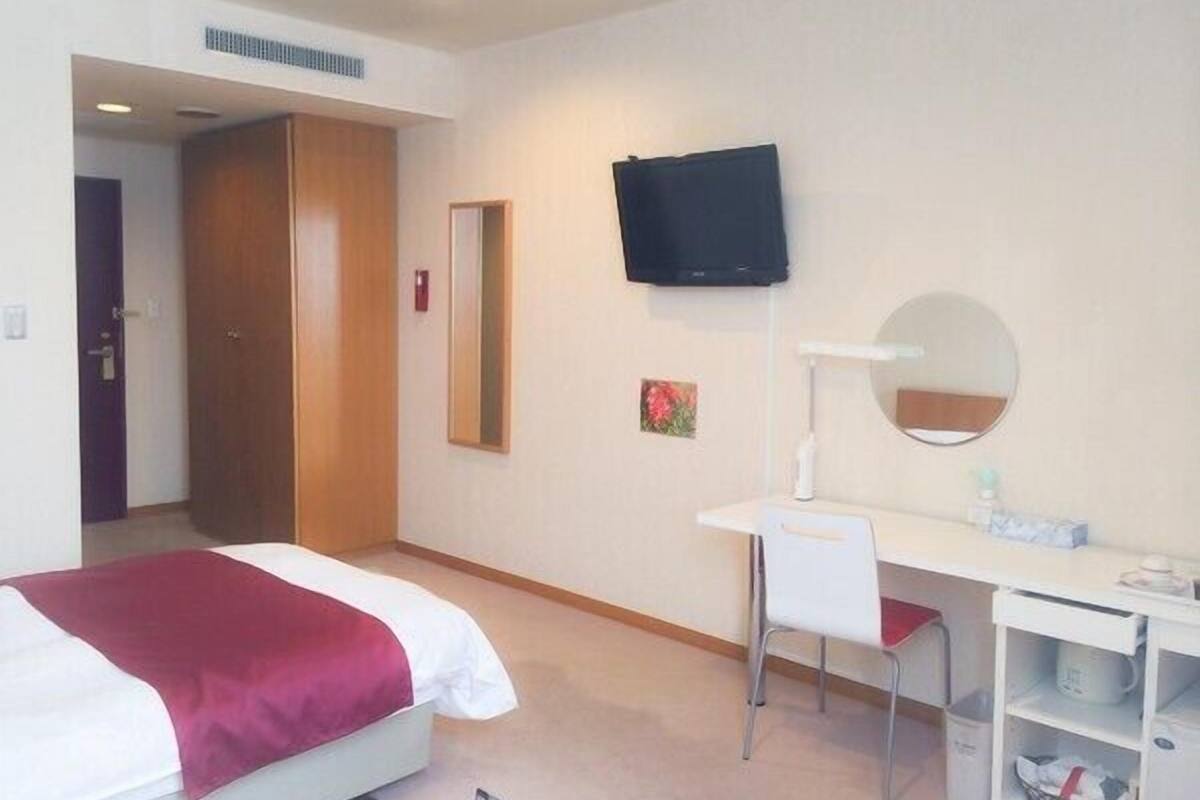 Ein Hotelzimmer mit Bett, Schreibtisch, Stuhl, Fernseher, Spiegel und Ablagefach für Toilettenartikel.