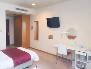 A hotel room with a bed, a desk, a chair, a television, a mirror, and a shelf with toiletries.