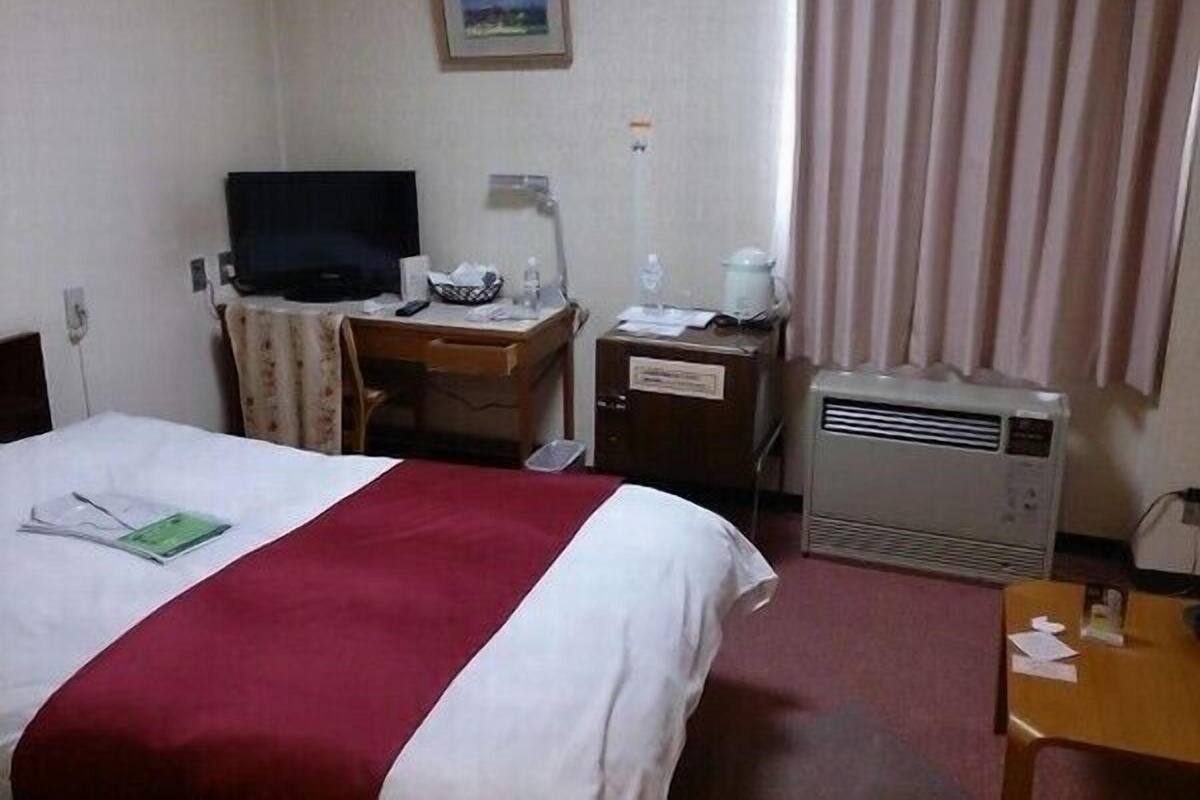 Ein Hotelzimmer mit Bett, Schreibtisch, Fernseher, Heizung und einem Fenster mit Vorhängen.