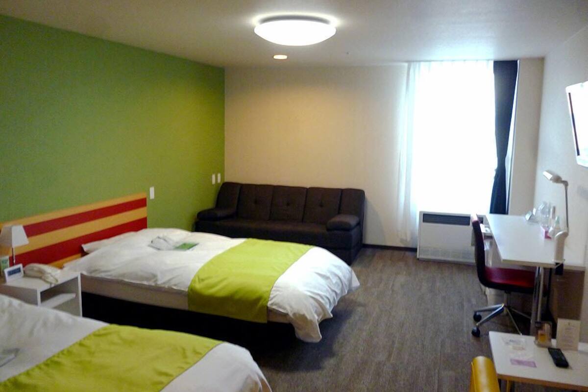 Ein Hotelzimmer mit zwei Betten, einem Sofa, einem Schreibtisch und einem Fernseher.