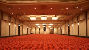 Une grande chambre d’hôtel vide, avec un tapis rouge, plusieurs portes et des lustres.