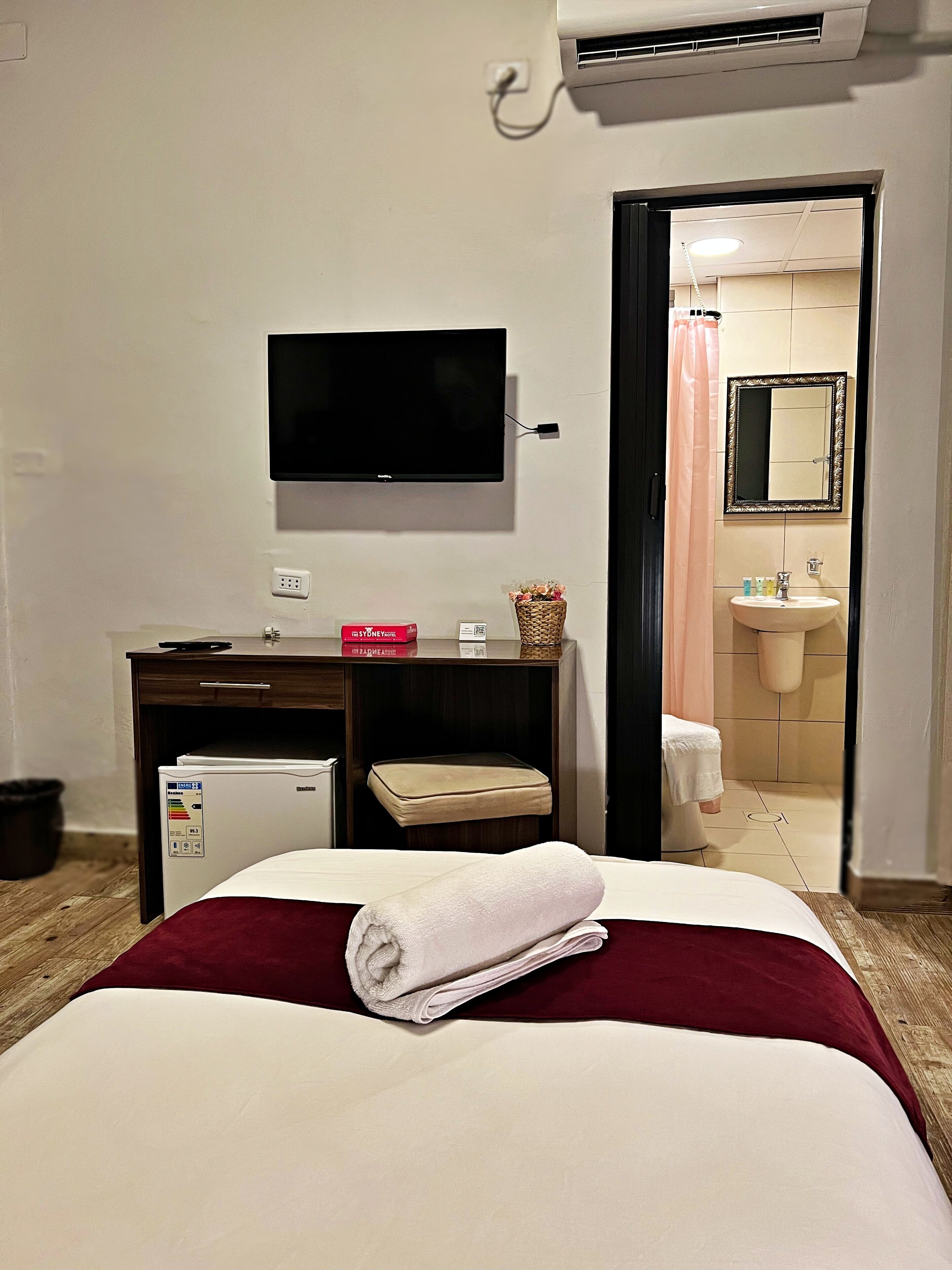A hotel room with a bed, a desk with a computer, a television, and a bathroom visible through an open door.