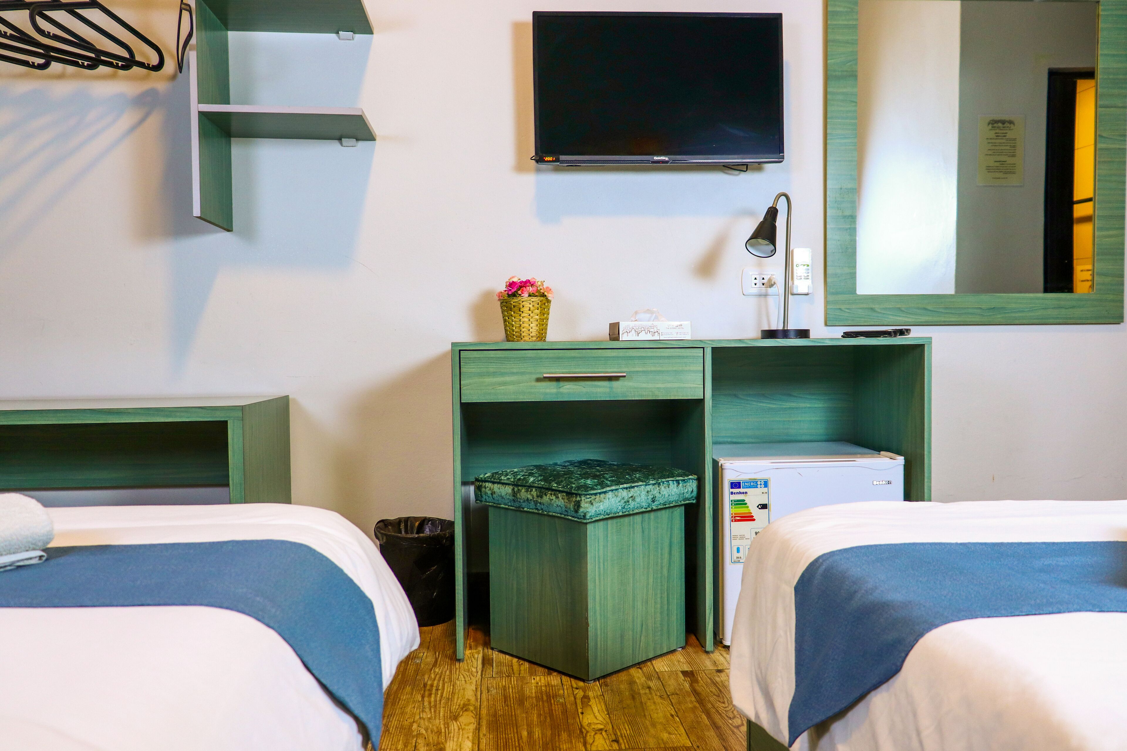 Hotelkamer met twee bedden, een televisie, een spiegel, een bureau met lamp en een prullenbak.