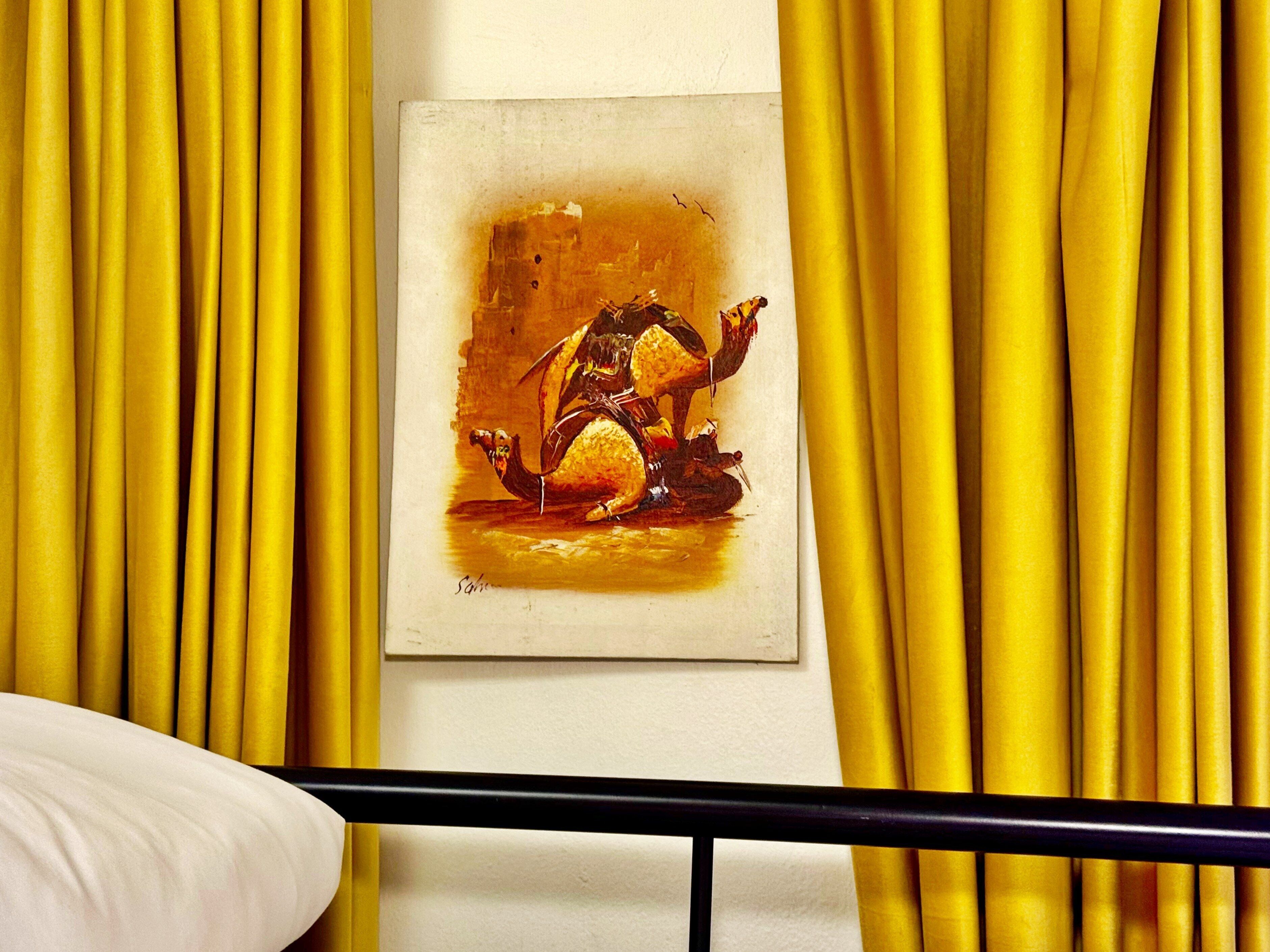 Una pintura de un camello en una pared, rodeada de cortinas amarillas.