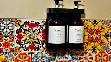A bathroom with a colorful tile backsplash and two bottles of Elyra shampoo and shower gel mounted on the wall.