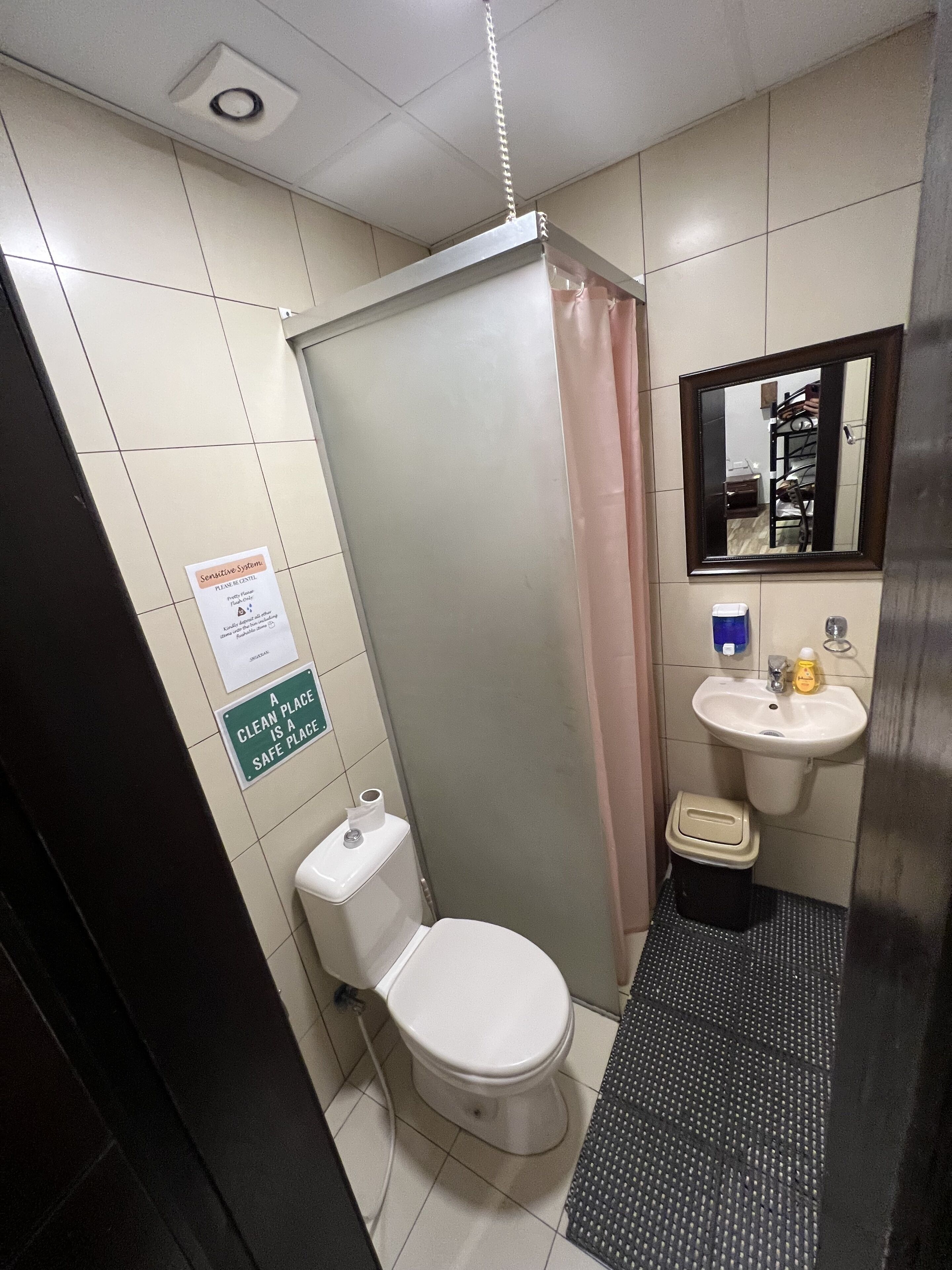 A small bathroom with a toilet, a sink, and a shower stall. There are signs on the wall indicating a clean place is a safe place.