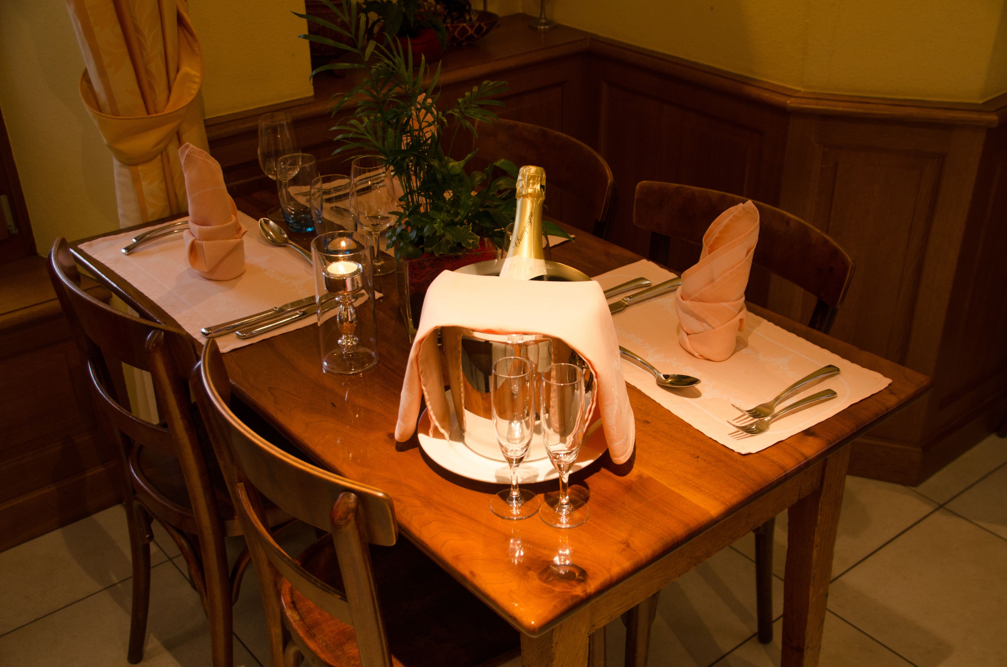 A dining table set with a bottle of champagne, two wine glasses, and a candle.