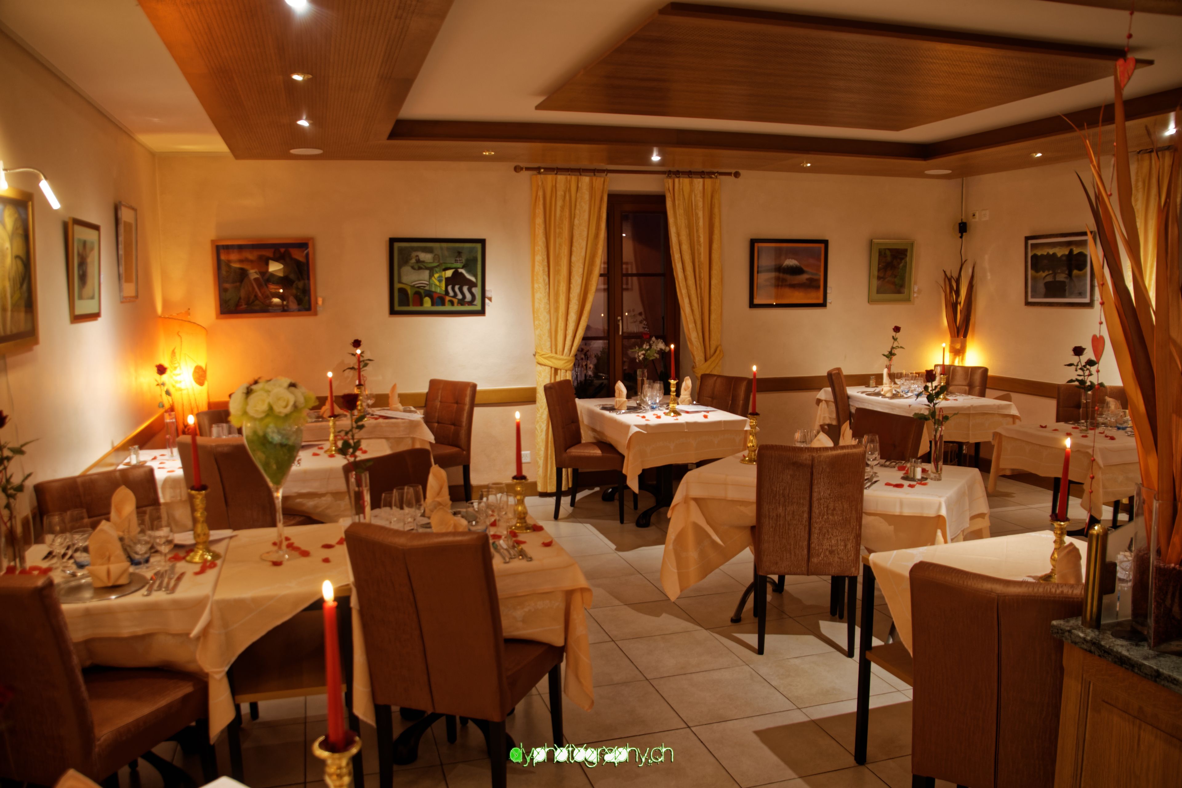 Restaurante com várias mesas preparadas para refeições, com velas e arranjos florais.
