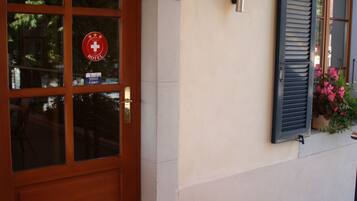 A hotel entrance with a wooden door, a number sign, and a window with shutters.
