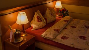 A hotel room with a bed, two bedside lamps, a nightstand with a bottle of champagne and a glass, and a floral-patterned bedspread. - Auberge Communale (Gilly)