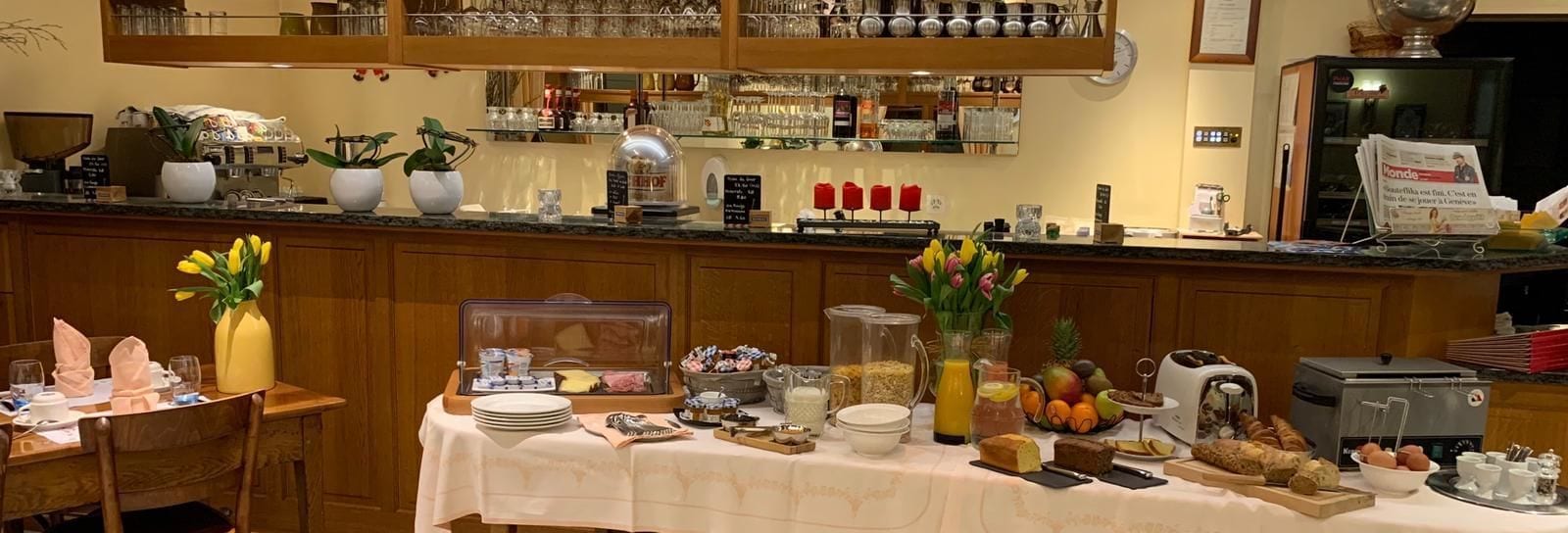 A breakfast buffet setup with various food items, a coffee machine, and a newspaper rack.