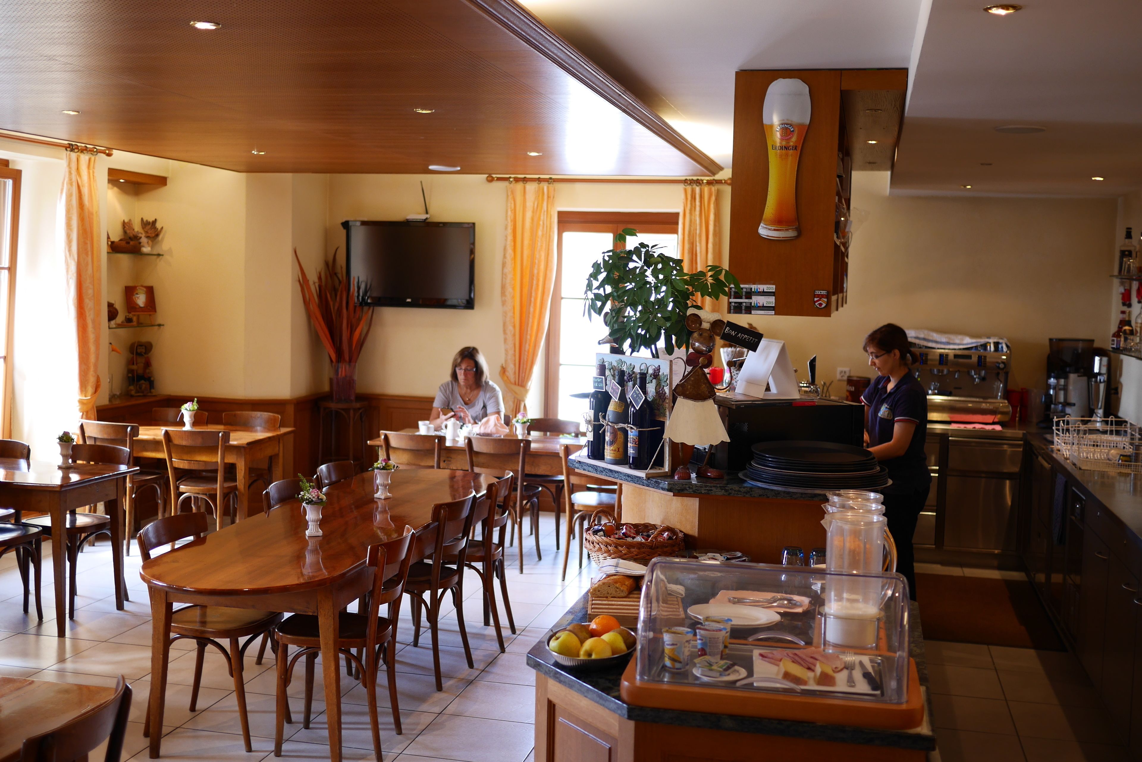 A restaurant with wooden tables and chairs, a buffet counter, and a television mounted on the wall.