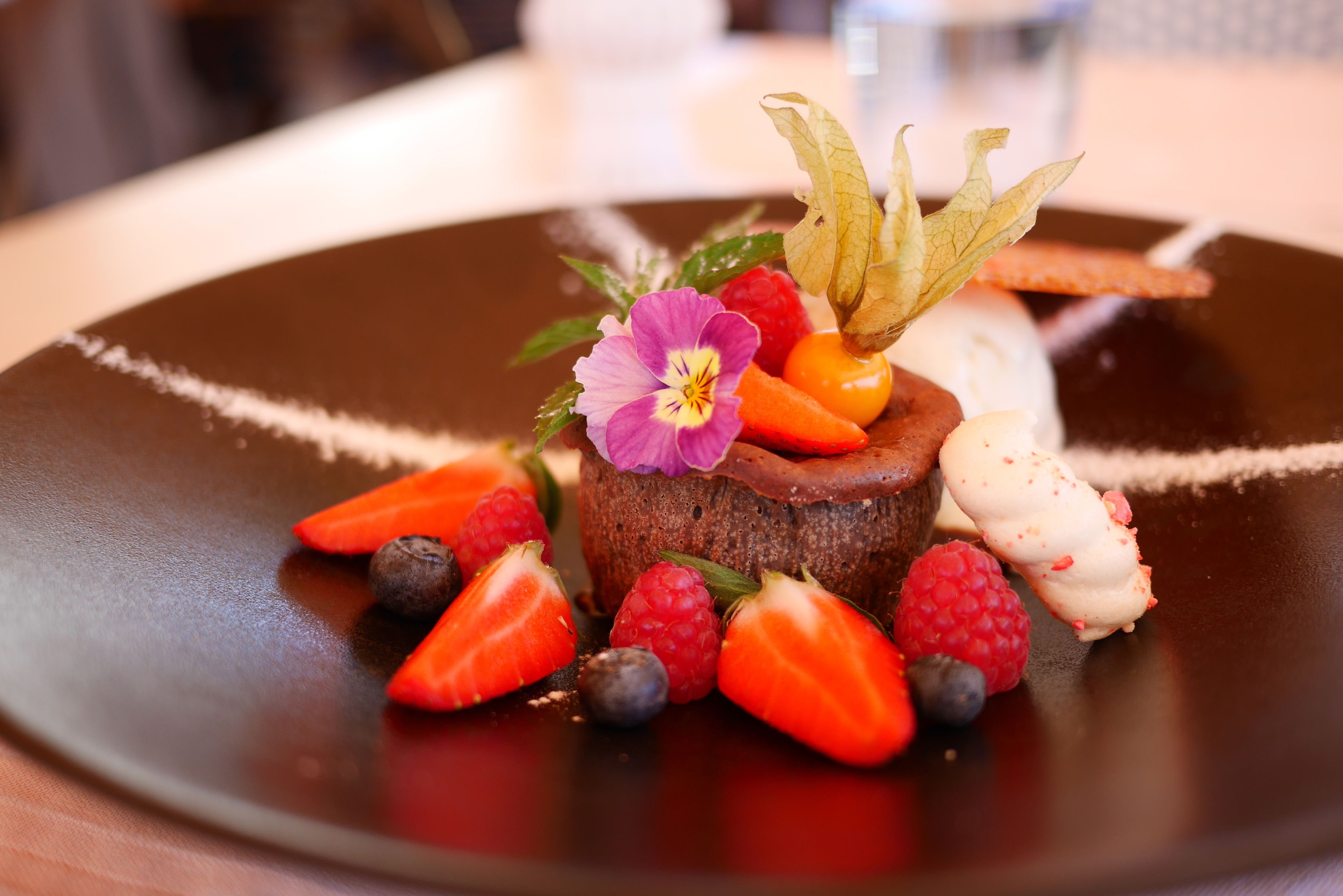 Ein Dessertteller mit Schokoladenkuchen, Erdbeeren, Himbeeren, Blaubeeren und einer violetten Blume.