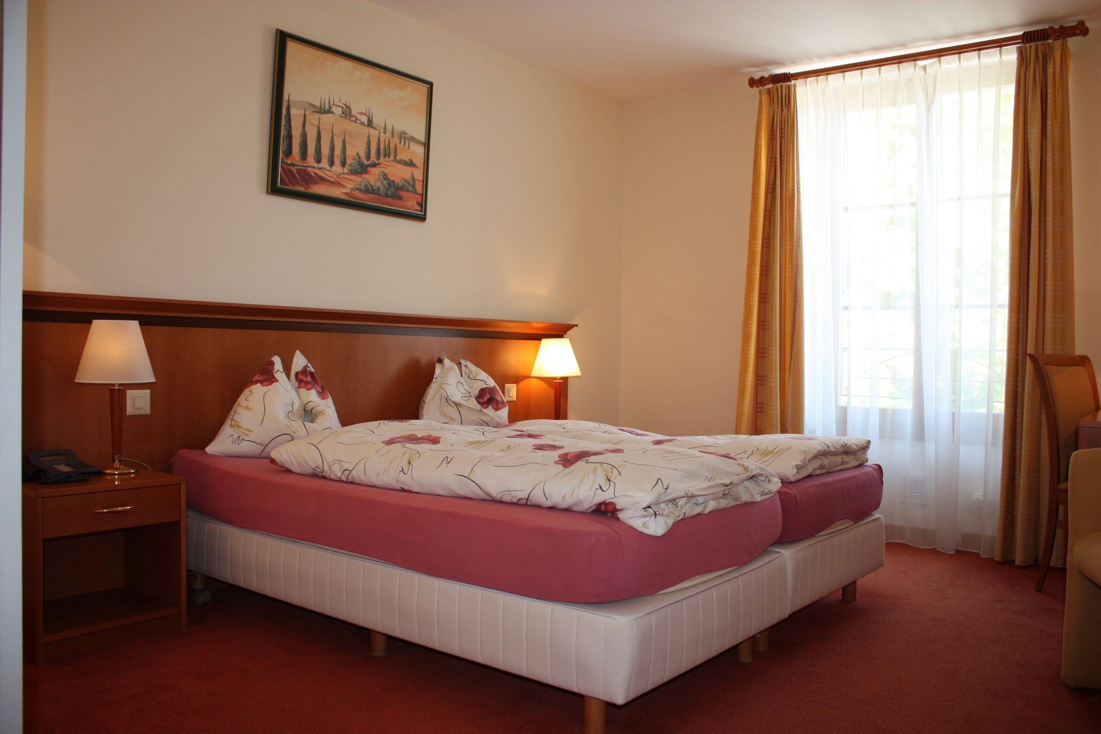 Une chambre d’hôtel avec un lit, deux lampes de chevet, une table de chevet, une chaise et une fenêtre avec des rideaux.